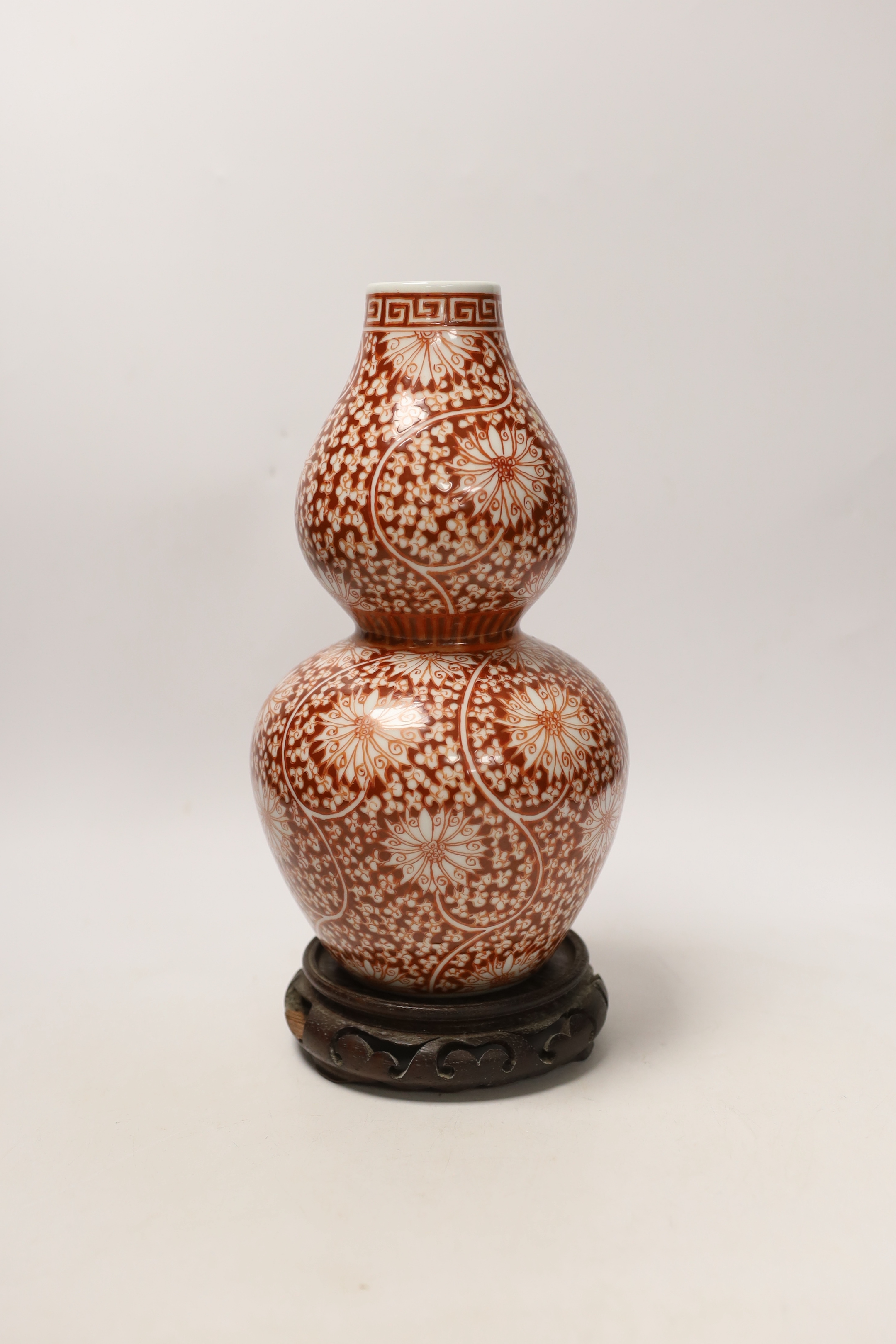 A Chinese iron-red double-gourd vase on hardwood stand, 29cm high